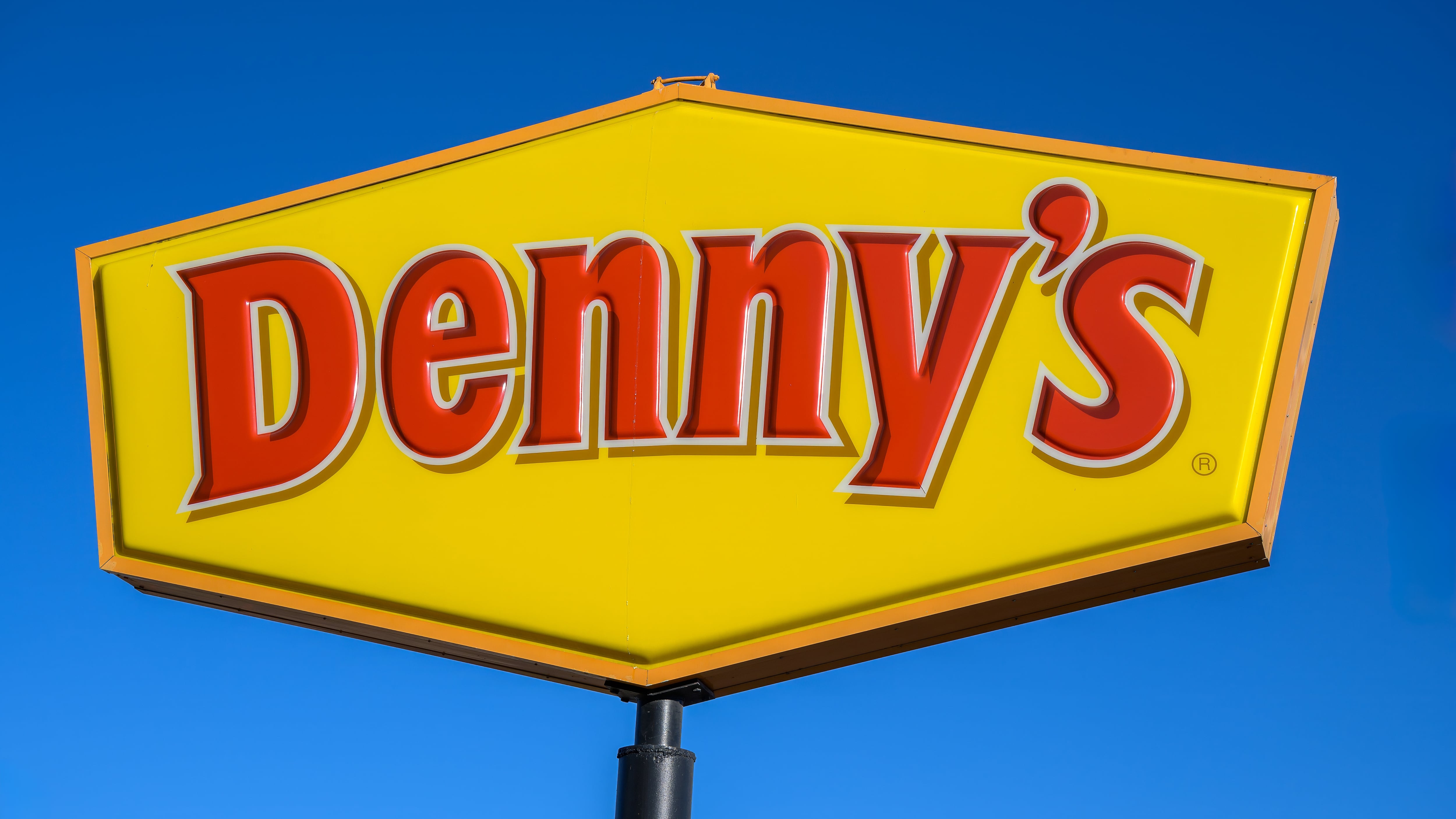 Denny's restaurant sign and logo against blue sky.
